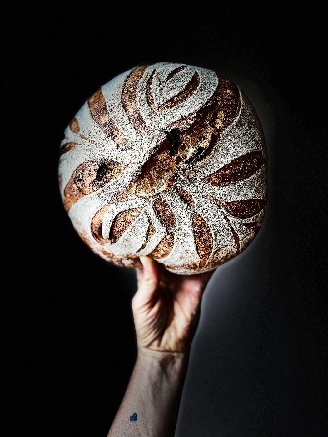 Sauerteiglaib mit eingeschnittenem Blattmuster, in einer Hand hochgehalten